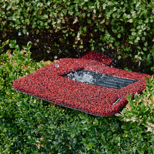 Red honeycomb car mat being rinsed with water outdoors