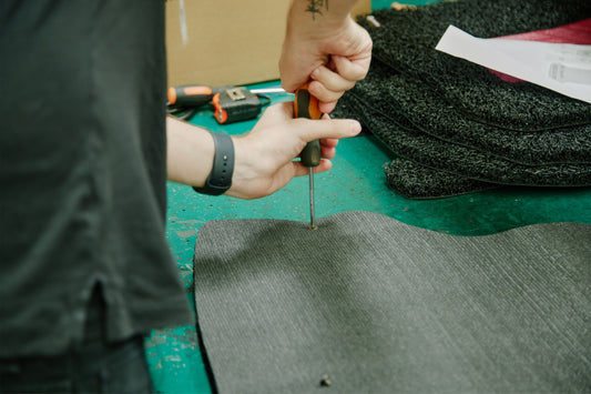 Worker trimming grey car mat material with scissors during production